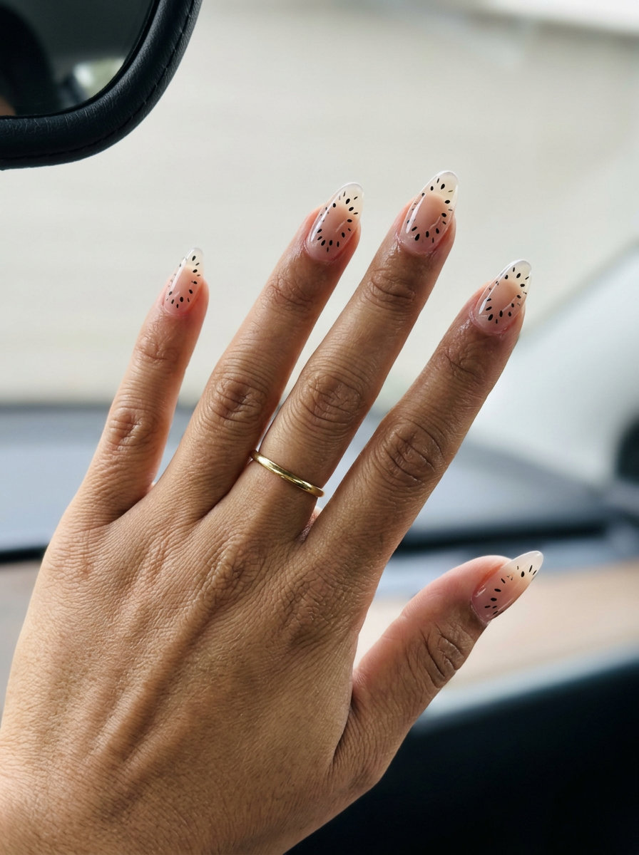 Artistic Kiwi Negative Space Almond nails featuring clear base with black seed accents for a modern date night look. Summer fruits nail art 2026.