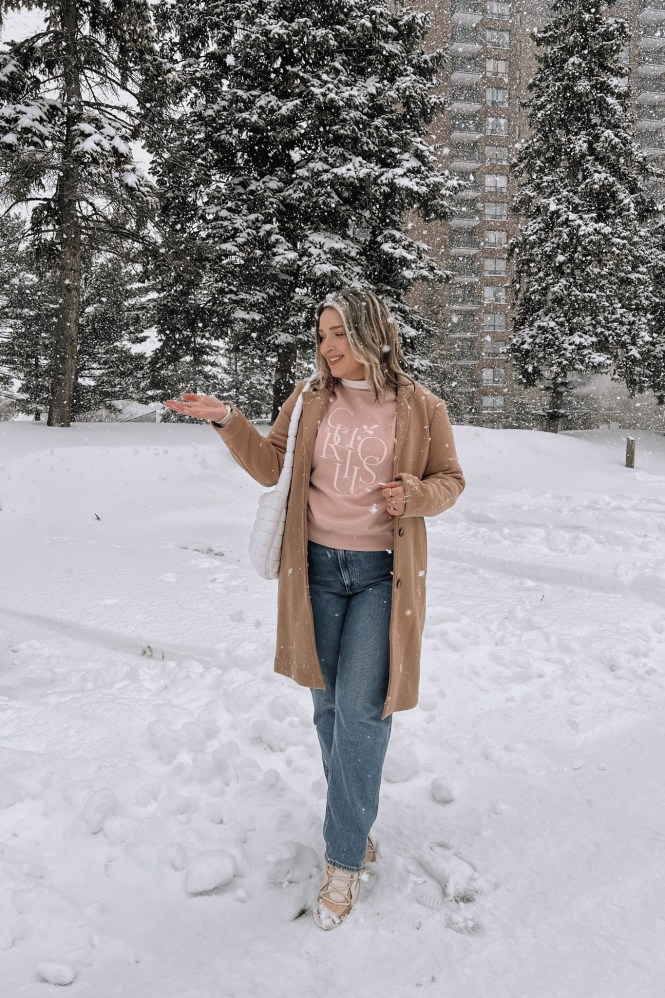 Camel Coat Over Graphic Sweatshirt and Jeans for a Casual Snow Day — Snow Day Outfits