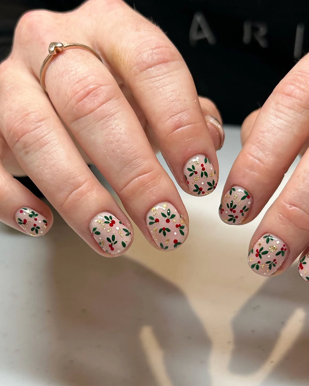 Short rounded nude pink nails with miniature red and green floral patterns