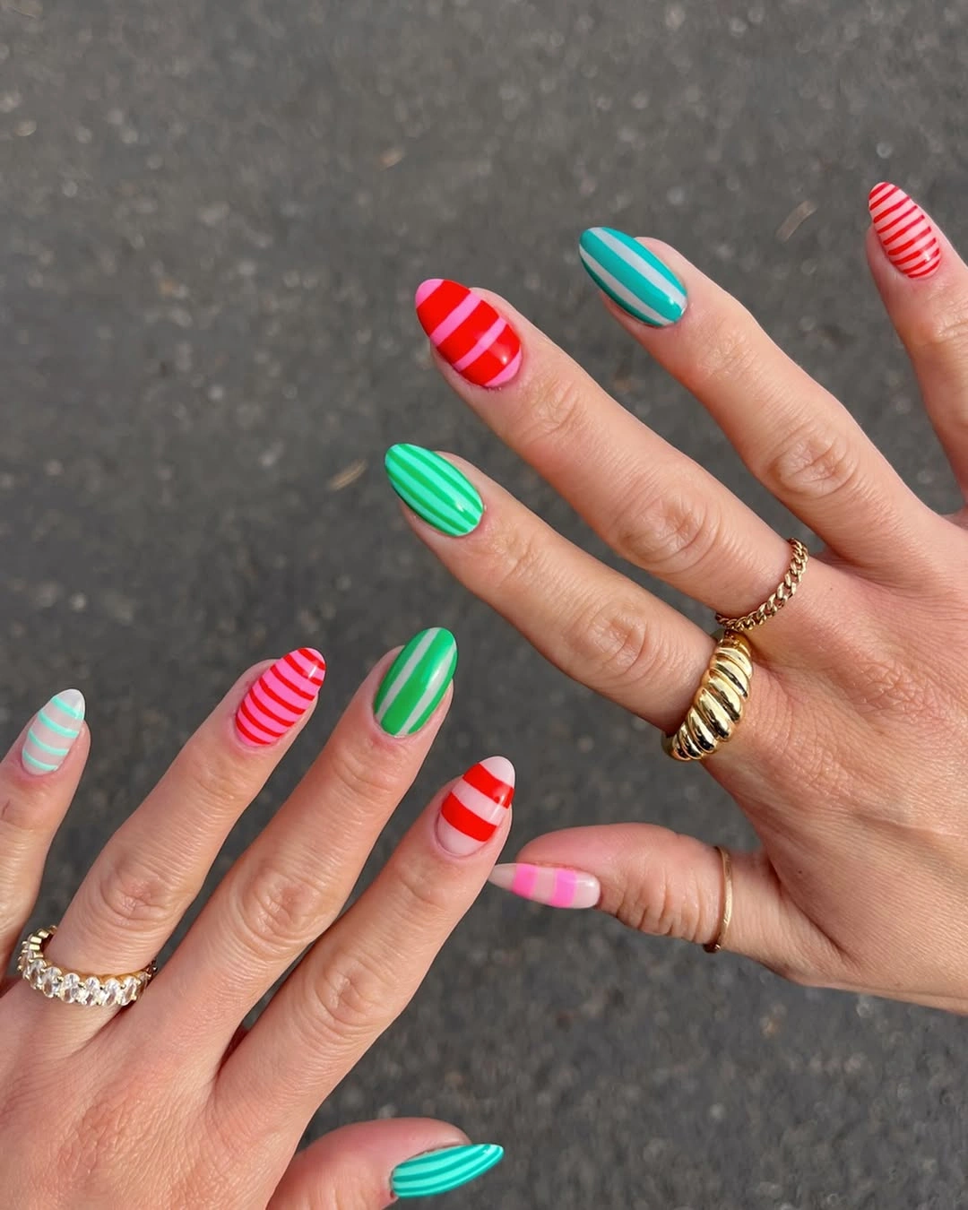 Two hands with red green turquoise pink and white striped nails
