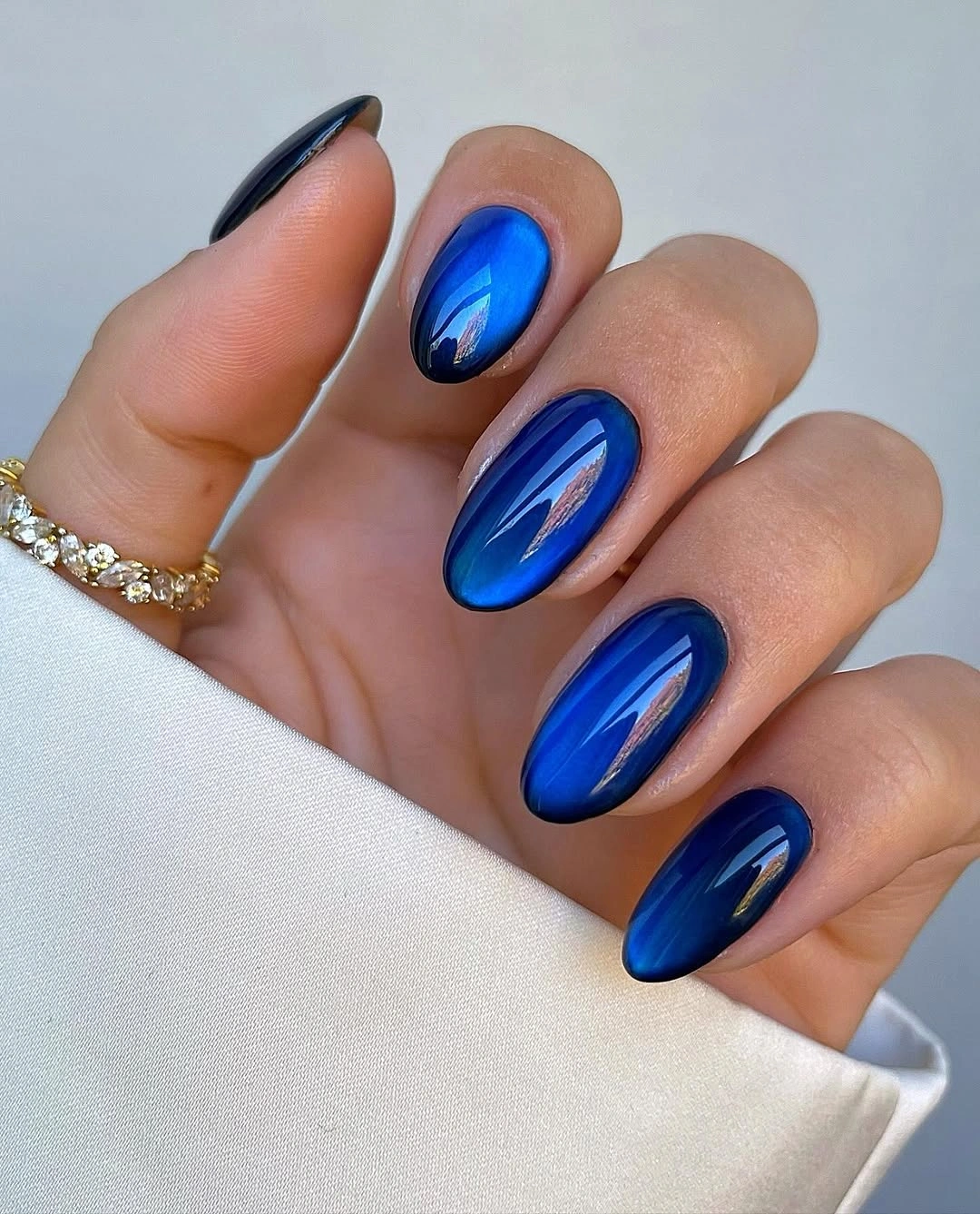 Glossy cobalt blue almond nails with dark navy edges and bright reflections